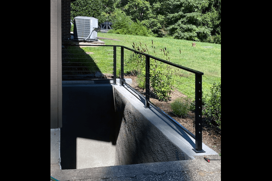 Black cable railing on outdoor staircase leading to a below ground room next to bushes
