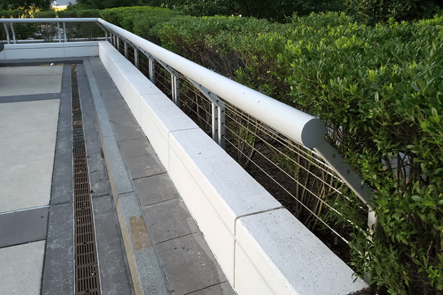 White metal cable railing outdoors with bent design in front of a bush