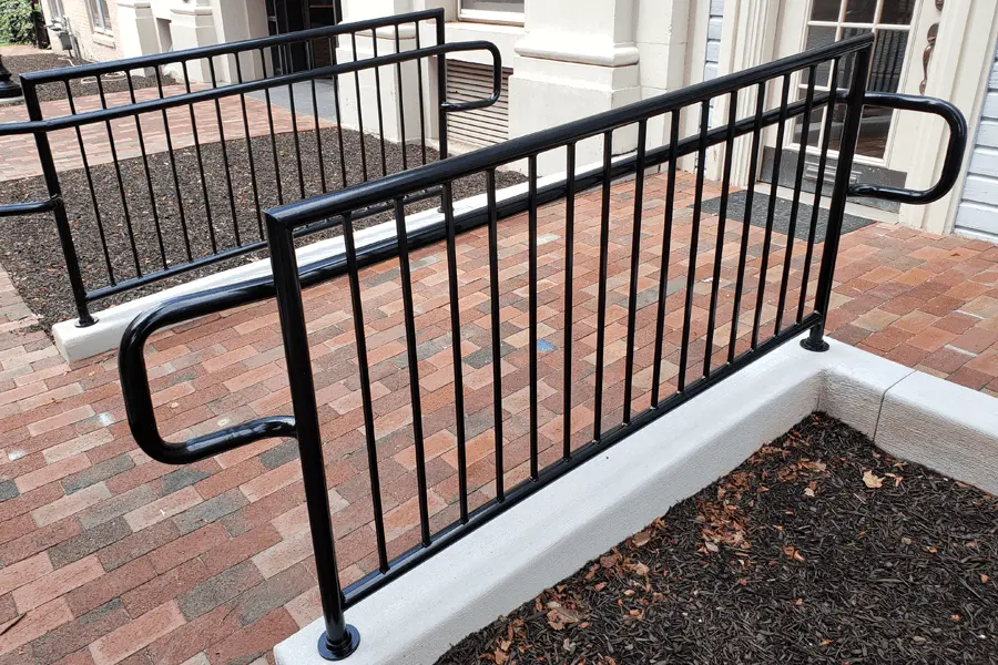 Photo of black metal commercial railing for outdoor brick ramp leading to a blue building