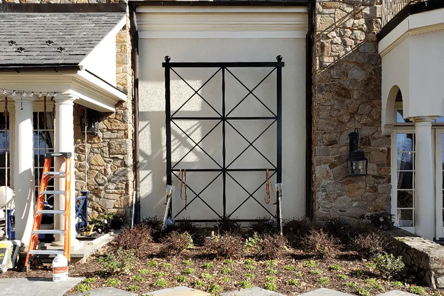 Photo of black decorative metalwork made of squares and 'x's being installed on the side of the house