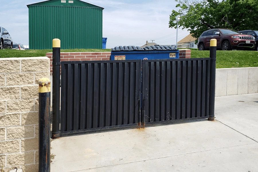 Photo of solid black welded metal panel gate with black posts with yellow tops