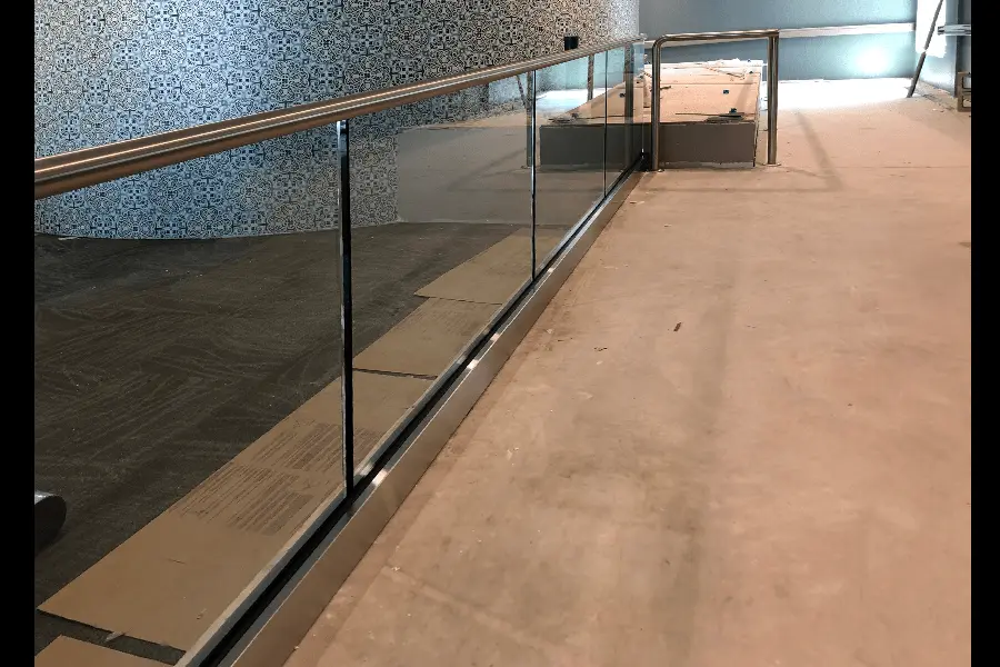 Photo of glass railing with metal bar on top in front of mosaic wall