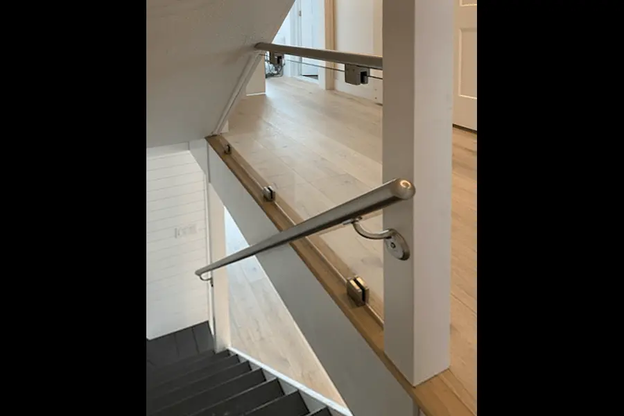 Photo of glass railing on indoor staircase with light brown wood floors and white walls