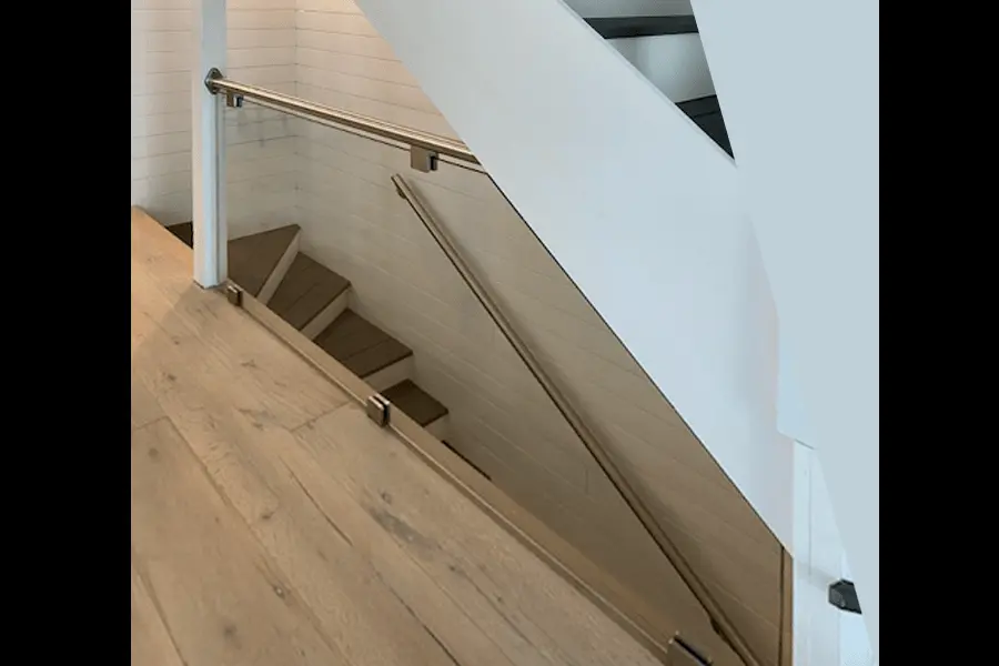 Photo of glass railing on indoor staircase with light brown wood floors, dark brown wood stairs and white walls