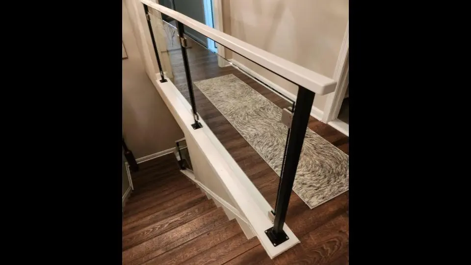Photo of residential glass railing on indoor staircase with black and white metal rails from a downwards view