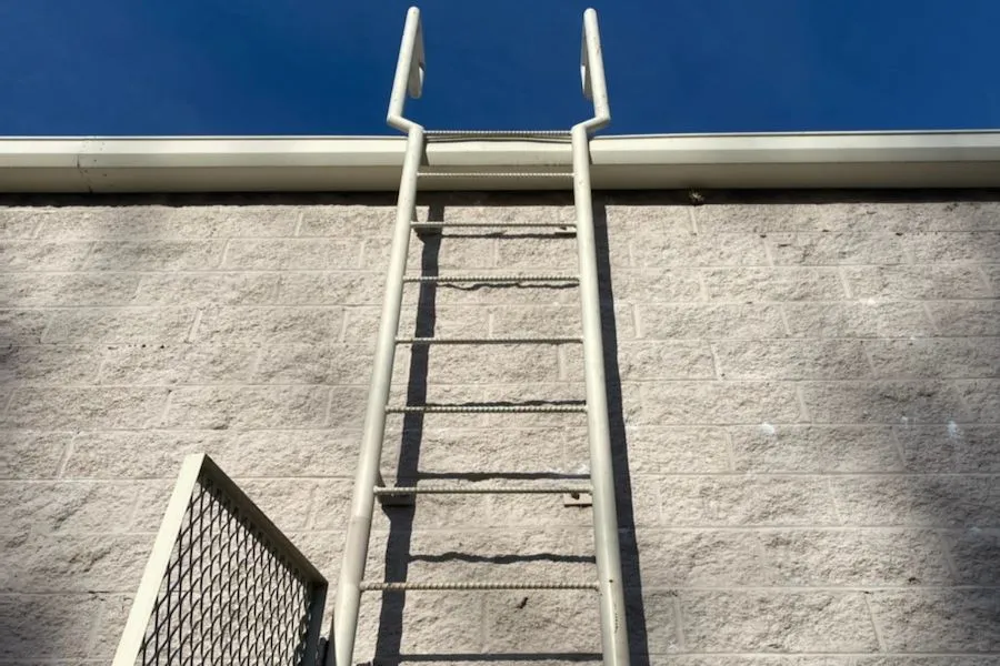 Photo of a White metal ladder attached to a wall and roof of a building with a metal side railing