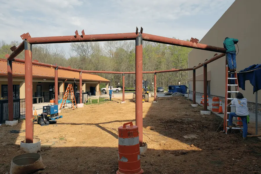 Photo of a red metal pipe permanent pavilion being installed outdoors in a Maryland shopping center, view from the front