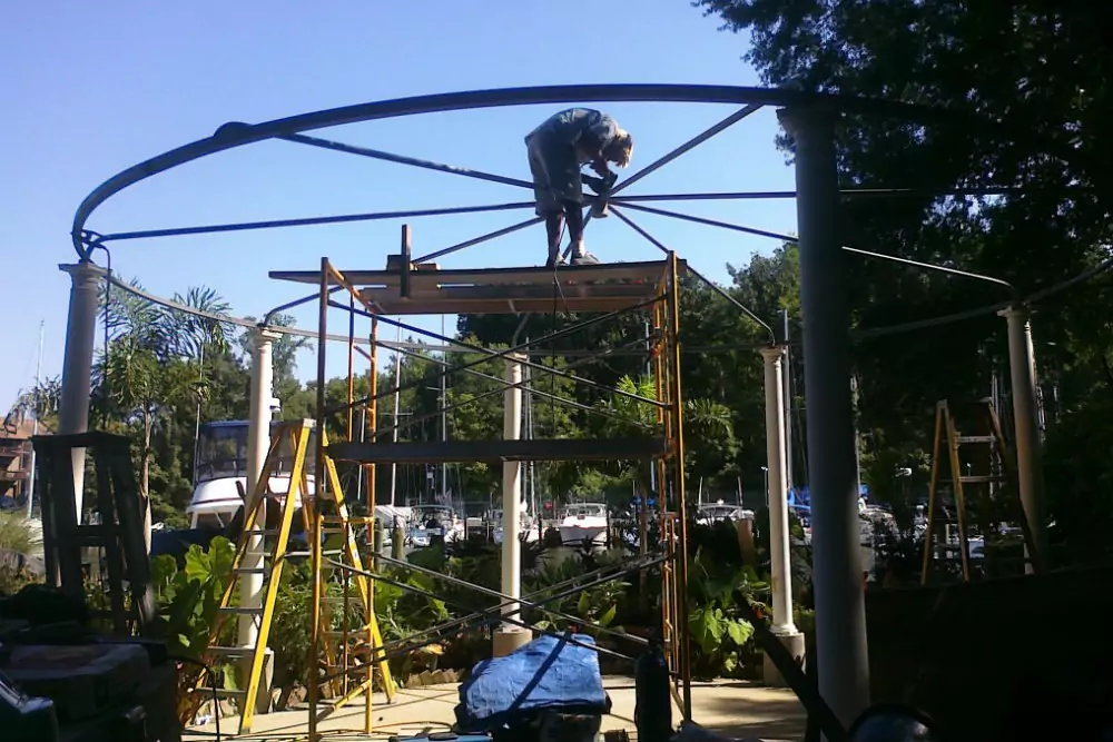 Photo of a white metal pavillion being built with boats in the background