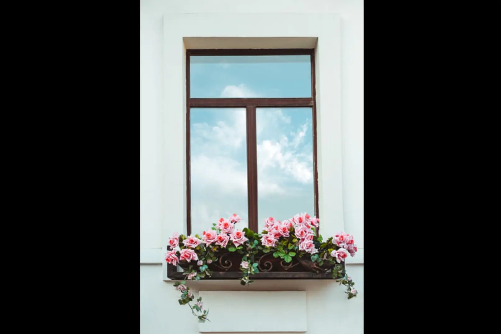 Photo of brown metal flower box attached to a window on a white building