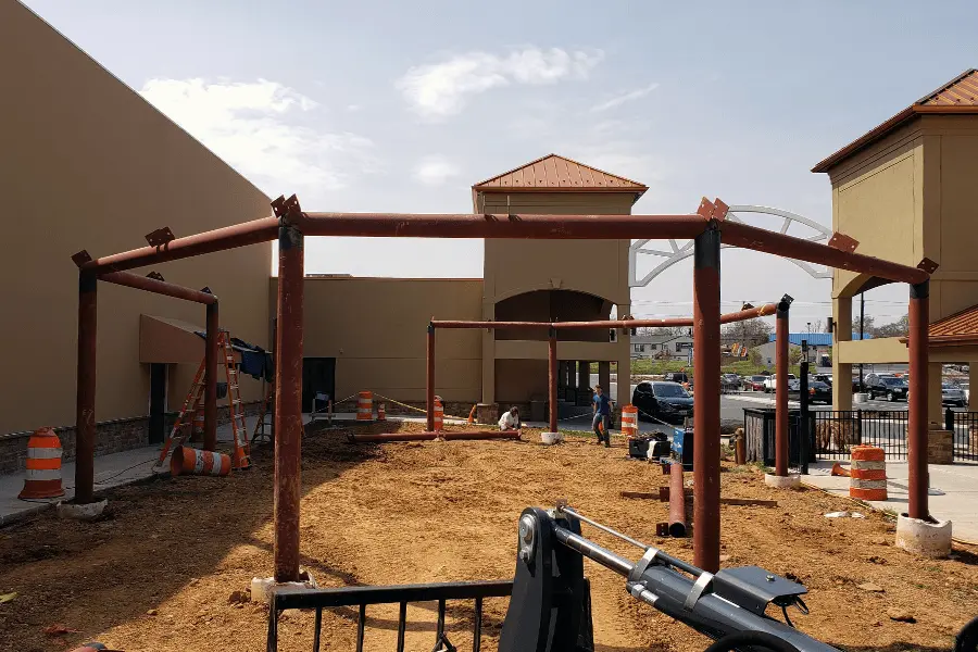Photo of a red metal pipe permanent pavilion being installed outdoors in a Maryland shopping center, view from the back