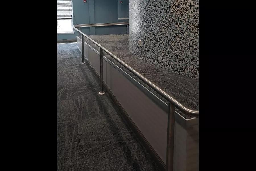 Photo of silver pipe railing wrapping around a corner in a carpeted room with blue walls