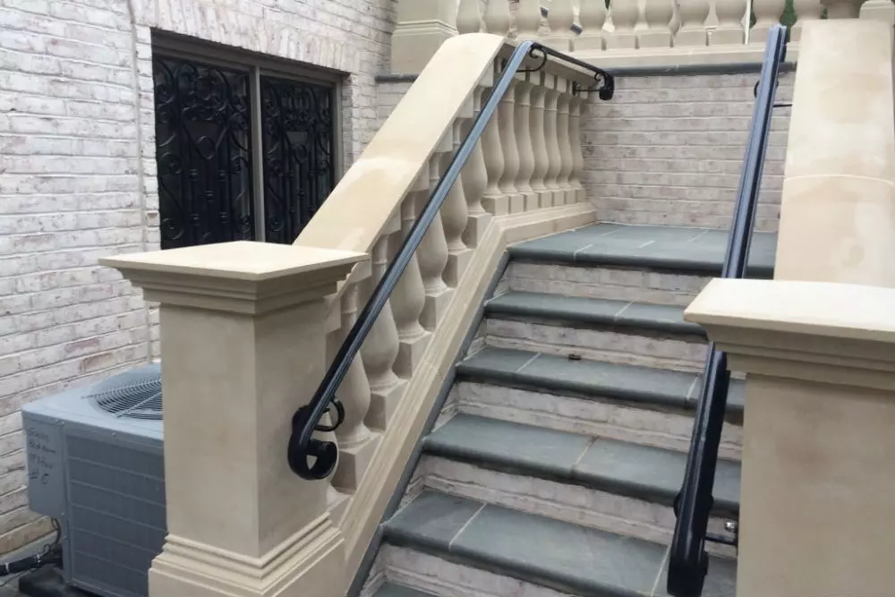 Photo of black metal railing on stone outdoor staircase in front of black metal decorative window bars