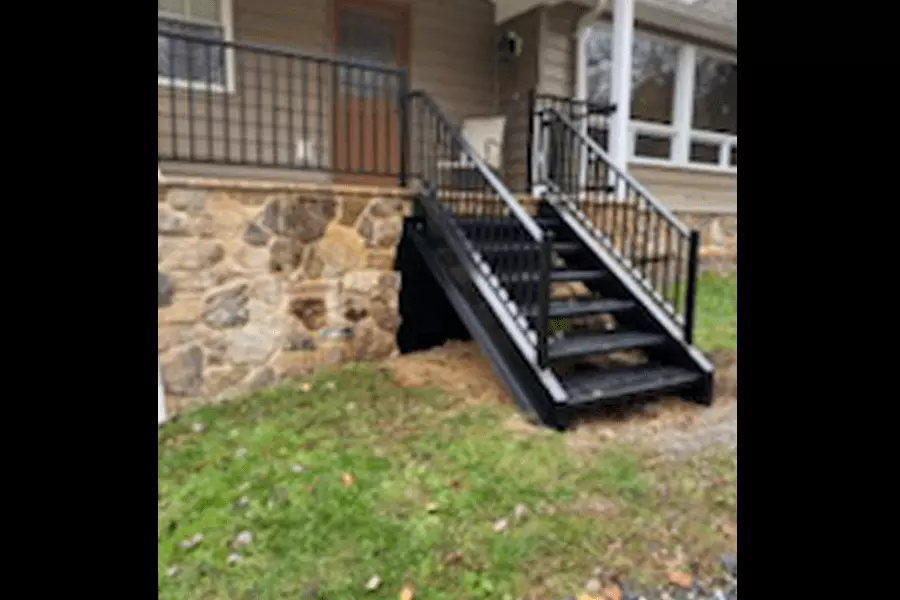Photo of black metal outdoor staircase with black railing leading up to a stone porch with black railing